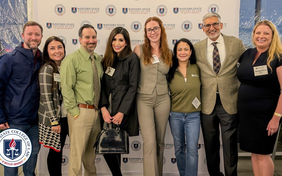 Eight attendees smiling in front of a Western State College of Law backdrop at the Fall 2026 Alumni Mixer. Western State logo seal overlayed.